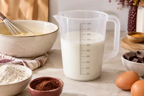 Verre doseur transparent APS d’un litre avec graduations et poignée, posé sur un plan de travail clair.
