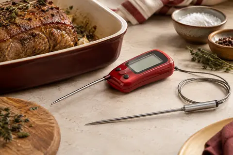 Thermomètre de cuisson rouge à double sonde posé près d’un rôti sur un plan de travail clair