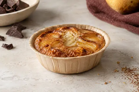 Mini tarte dorée dans un moule individuel en papier non blanchi, sur un plan de travail clair.