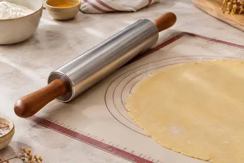 Rouleau à pâtisserie en inox avec poignées en bois posé sur un tapis de silicone gradué.