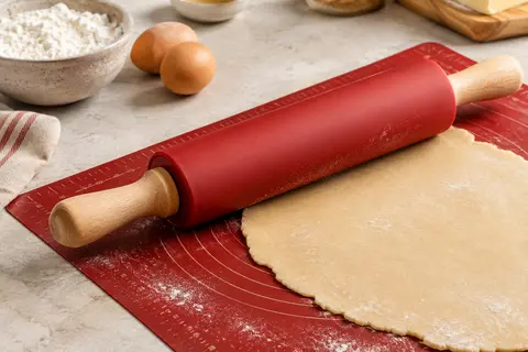 Rouleau rouge en silicone avec poignées en bois posé sur un tapis de pâtisserie gradué