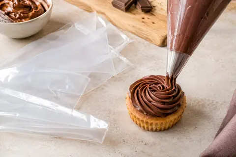 Poche à douille transparente remplie de crème cacao, avec des poches jetables posées sur un plan de travail clair.