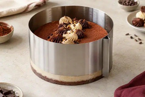 Cercle à pâtisserie extensible en inox avec graduations, posé autour d’un gâteau sur un plan de travail clair.