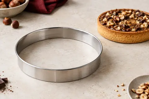 Cercle à tarte rond en inox posé près d’une tarte sur un plan de travail en pierre claire.