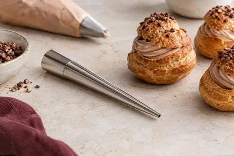 Douille à garnir en acier inoxydable posée près de choux sur un plan de travail clair