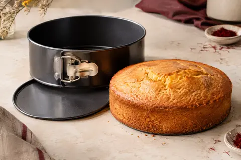 Moule à manqué rond en acier noir avec charnière, accompagné d’un gâteau démoulé sur un plan clair.