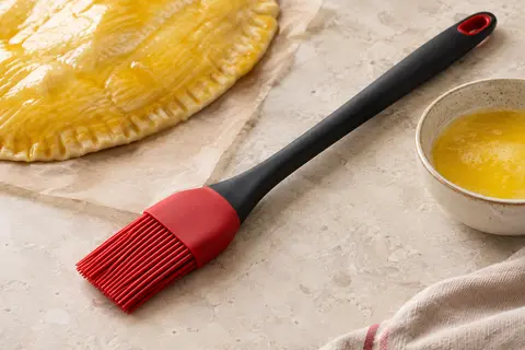 Pinceau de cuisine en silicone rouge et noir posé près d’une pâte dorée sur un plan de travail clair