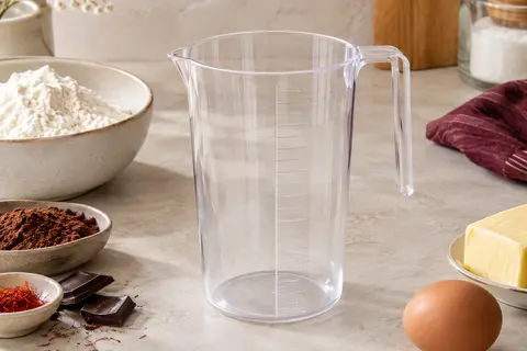 Verre doseur transparent Fackelmann d’un litre posé sur un plan de travail clair près d’ingrédients de pâtisserie