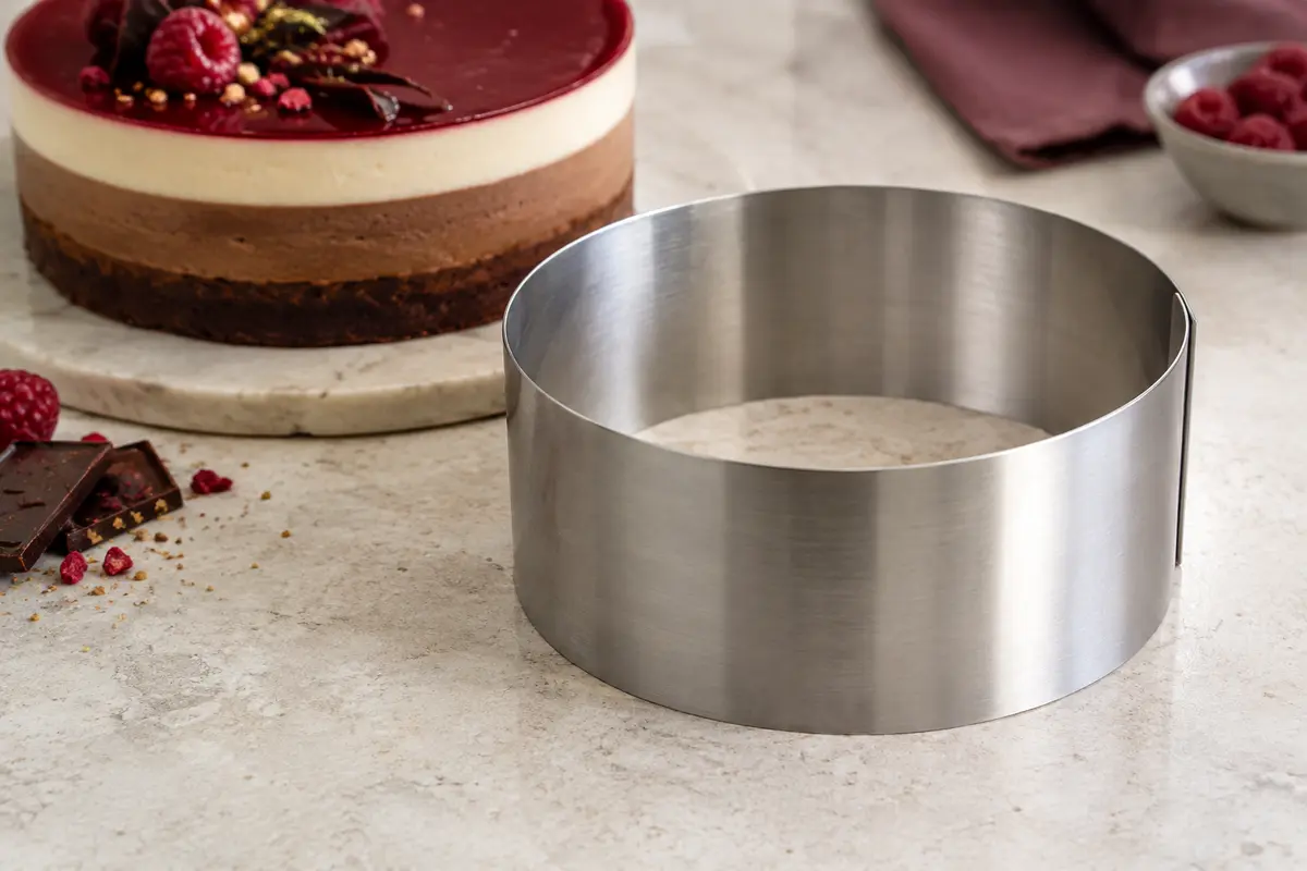 Cercle à pâtisserie en inox posé à côté d’un entremets rond à plusieurs couches