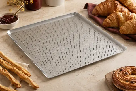 Plaque de cuisson rectangulaire en aluminium perforé posée près de baguettes et de viennoiseries dorées