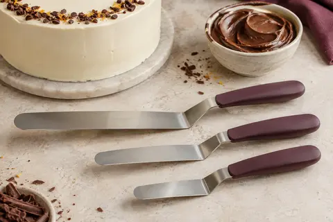 Trois spatules coudées en acier inoxydable et plastique PP posées près d’un gâteau glacé