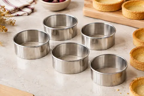 Six cercles à tartelettes ronds en inox à bord roulé, posés près de fonds de pâte cuits
