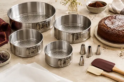 Quatre moules ronds à fond amovible accompagnés d’accessoires de pâtisserie sur un plan clair.