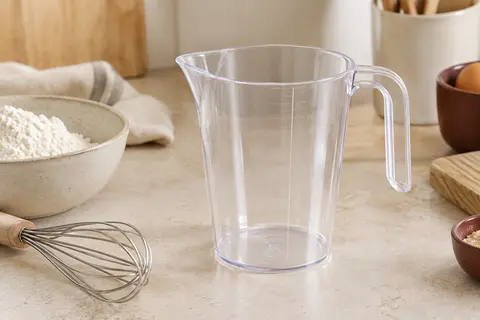 Verre doseur transparent en polypropylène avec poignée ouverte, posé sur un plan de travail clair.