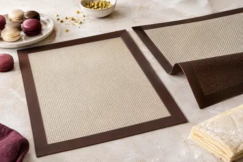 Deux tapis de cuisson micro-perforés avec des macarons et une préparation feuilletée sur un plan clair