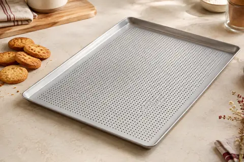 Plaque de pâtisserie perforée en acier gris argenté avec rebords, posée près de biscuits dorés.
