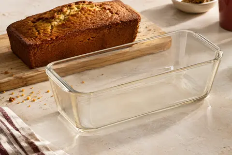 Moule à cake Pyrex en verre borosilicate transparent posé près d’un cake doré sur une pierre claire.