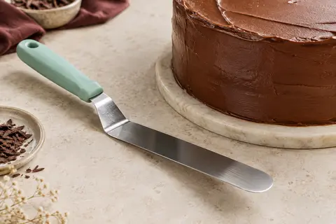 Spatule coudée ScrapCooking en inox posée près d’un gâteau glacé sur un plan clair.