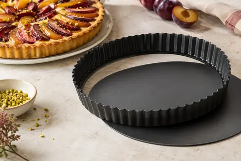 Moule à tarte rond noir à bords cannelés et fond amovible, posé près d’une tarte aux fruits