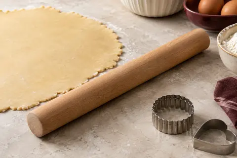 Rouleau à pâtisserie en bois de hêtre posé près d’une pâte à tarte étalée sur un plan clair