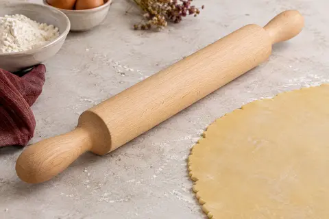 Rouleau à pâtisserie en hêtre massif posé près d’une pâte étalée sur un plan de travail clair