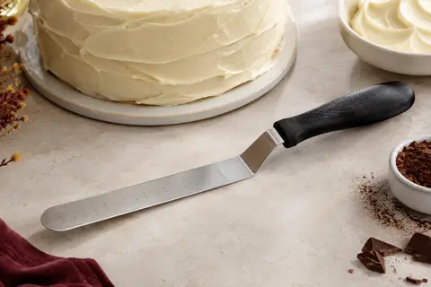 Spatule coudée en acier inoxydable graduée, posée près d’un gâteau couvert de crème lisse