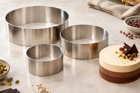 Trois cercles à pâtisserie en acier inoxydable de diamètres différents près d’un entremets mousse