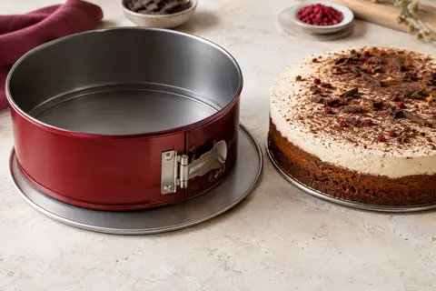 Moule à charnière rond rouge ouvert à côté d’un gâteau posé sur son fond métallique