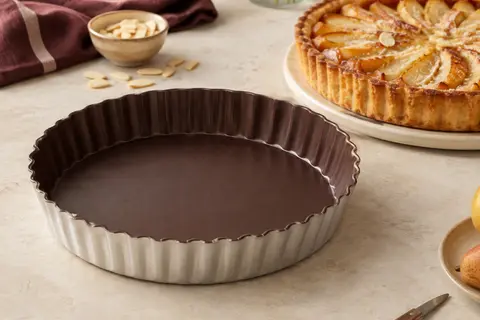 Moule à tarte rond Tefal en aluminium recyclé, finition chocolat, posé près d’une tarte dorée.