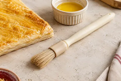 Pinceau à pâtisserie Thermohauser à poils naturels et manche ivoire posé près d’une pâte feuilletée