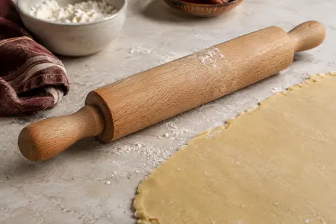 Rouleau à pâtisserie en hêtre posé près d’une pâte abaissée sur un plan de travail clair.
