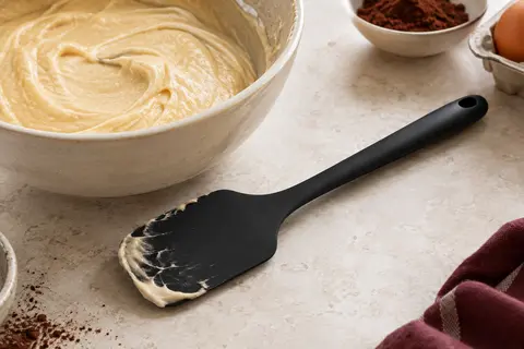 Maryse noire en silicone posée près d’un bol de pâte à gâteau sur un plan de travail clair