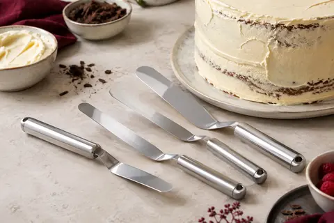 Spatules coudées en acier inoxydable près d’un gâteau à glaçage crème sur un plan clair.