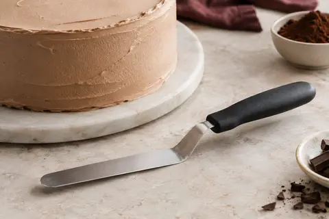 Spatule coudée Westmark à lame argentée et poignée noire posée près d’un gâteau à la crème