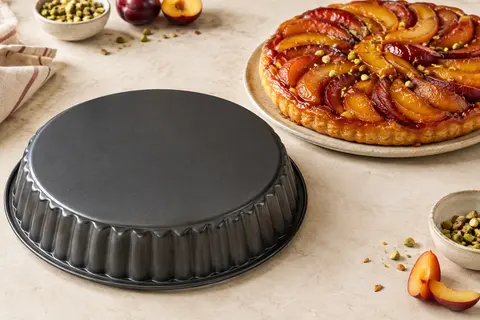 Moule à tarte renversée en acier antiadhésif posé sur un plan clair près d’une tarte aux fruits.