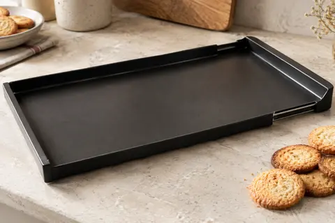 Plaque de cuisson extensible en acier noir posée sur un plan de travail clair près de biscuits